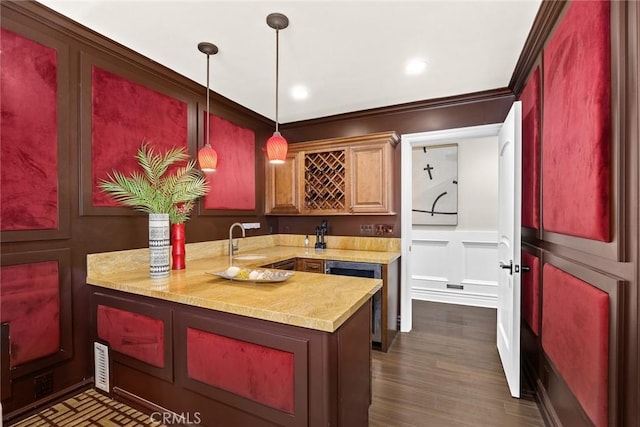 kitchen featuring kitchen peninsula, dark hardwood / wood-style flooring, crown molding, sink, and pendant lighting