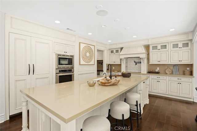 kitchen with custom range hood, dark hardwood / wood-style flooring, appliances with stainless steel finishes, and a large island