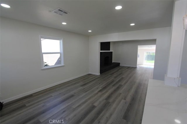 unfurnished living room with a fireplace, a healthy amount of sunlight, and dark hardwood / wood-style floors