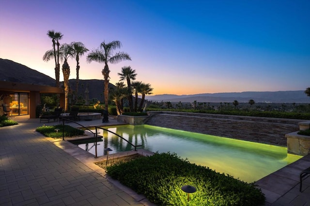 pool at dusk featuring a patio area, a mountain view, and a jacuzzi