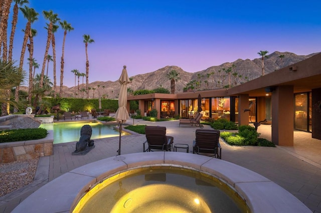 pool at dusk with a mountain view, a patio area, and an in ground hot tub