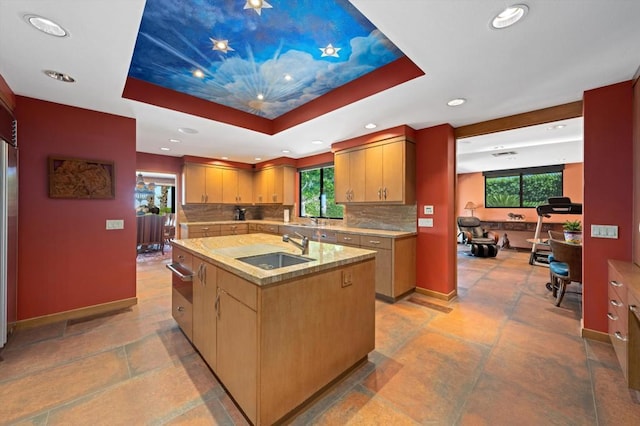 kitchen featuring sink, a kitchen island with sink, tasteful backsplash, and a tray ceiling