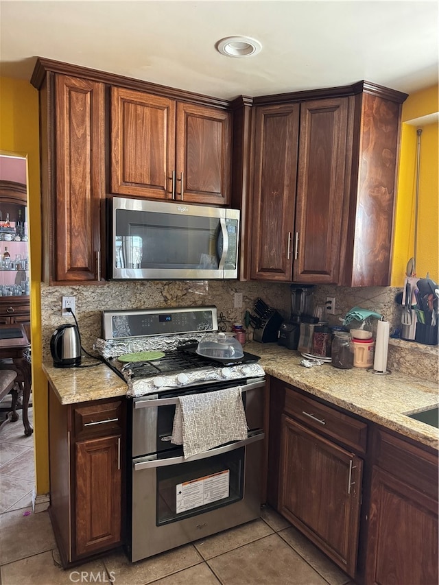 kitchen featuring light stone countertops, stainless steel appliances, backsplash, and light tile patterned floors