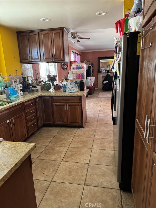 kitchen with ornamental molding, kitchen peninsula, ceiling fan, stainless steel refrigerator, and light tile patterned floors