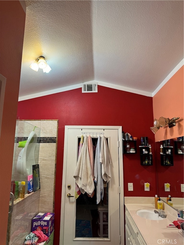 bathroom featuring vanity, lofted ceiling, a textured ceiling, and ornamental molding