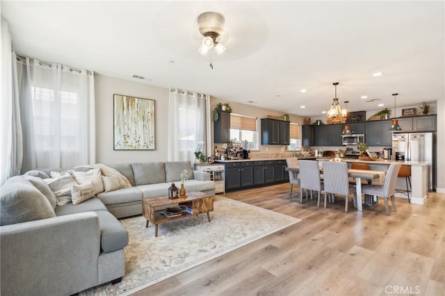 living room with light wood-type flooring, visible vents, recessed lighting, and ceiling fan with notable chandelier