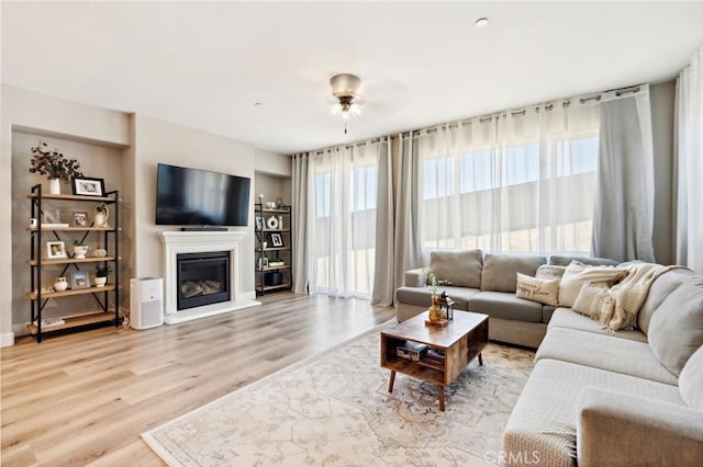 living room featuring a glass covered fireplace, baseboards, and wood finished floors