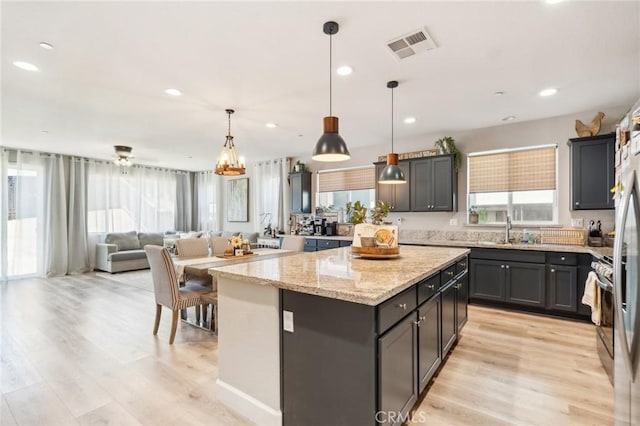 kitchen with visible vents, light wood-style flooring, a kitchen island, light stone counters, and a sink