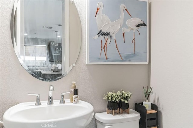 bathroom with visible vents, a textured wall, a sink, and toilet