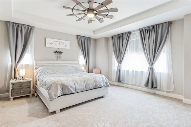 bedroom with a raised ceiling, carpet flooring, ceiling fan, and baseboards