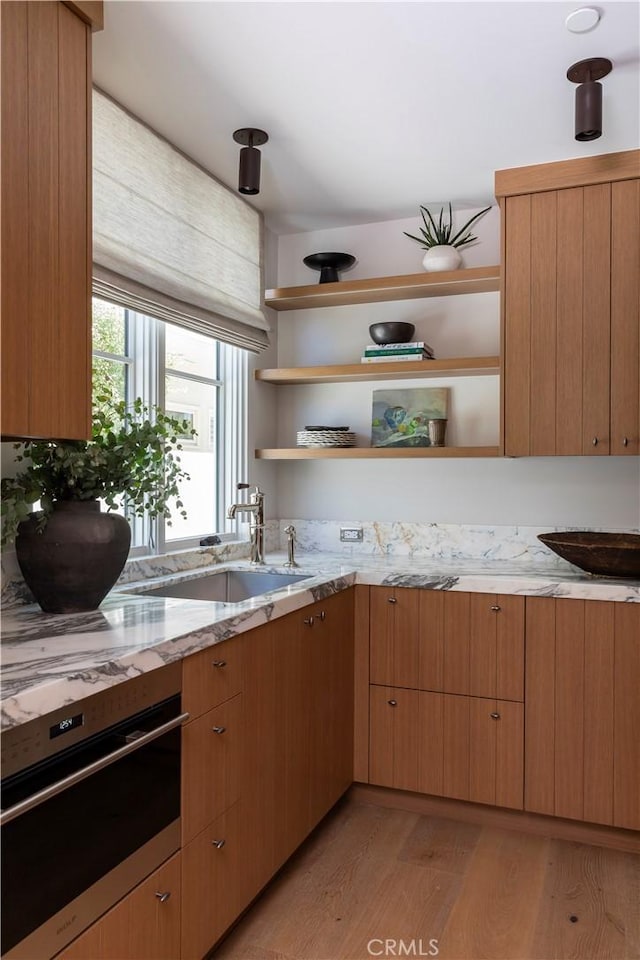 kitchen featuring light stone countertops, sink, stainless steel oven, and light hardwood / wood-style floors