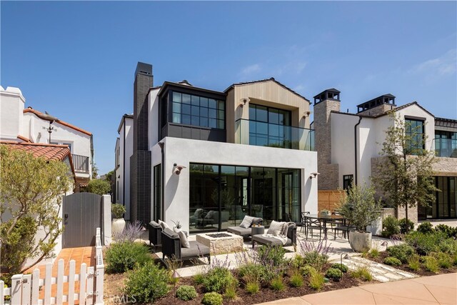 back of house with a balcony, a patio, and an outdoor living space with a fire pit