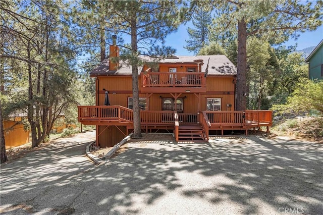 exterior space featuring a chimney, a wooden deck, and a balcony