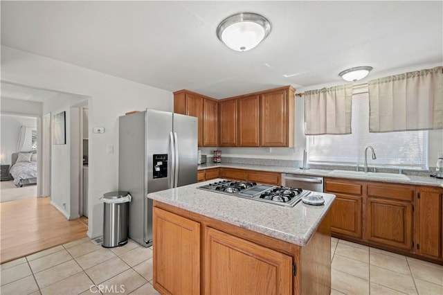 kitchen featuring stainless steel appliances, a sink, light tile patterned flooring, a center island, and brown cabinetry