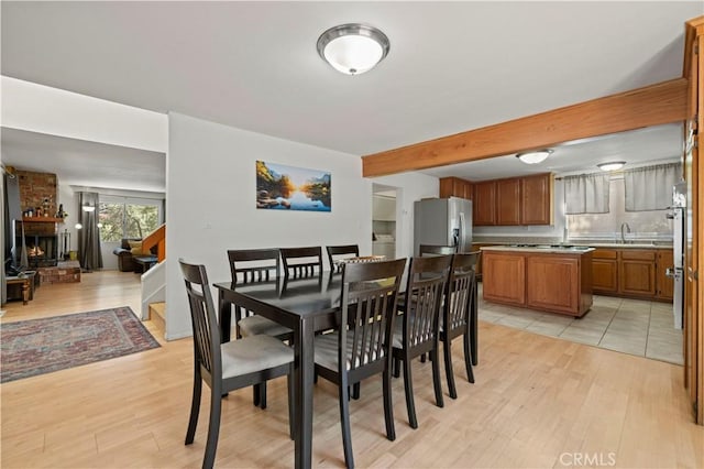 dining room with beam ceiling, a brick fireplace, and light wood-style floors
