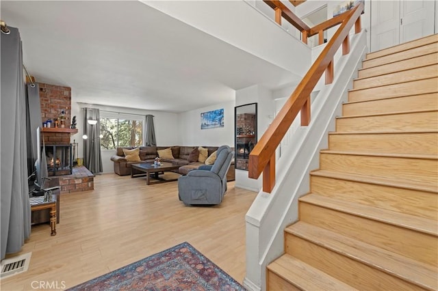 living room featuring wood finished floors, visible vents, stairs, and a brick fireplace
