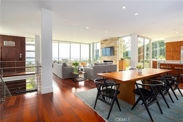 dining space featuring a large fireplace, dark wood-style floors, expansive windows, and a wealth of natural light
