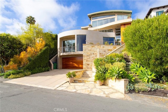 view of front of property featuring driveway, stone siding, stucco siding, a balcony, and a garage