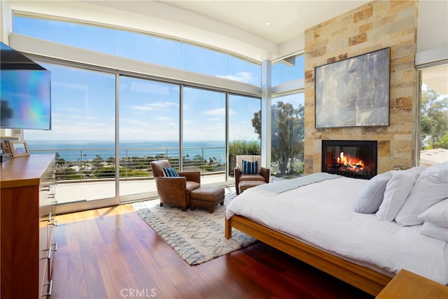 bedroom with a large fireplace, a water view, access to outside, and wood-type flooring