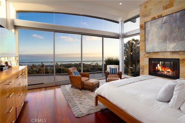 bedroom featuring a water view, wood finished floors, and a tile fireplace