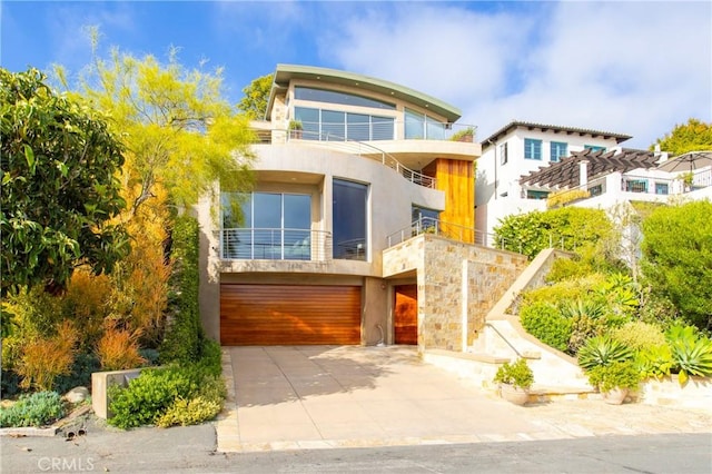 modern home featuring stucco siding, an attached garage, stone siding, a balcony, and driveway