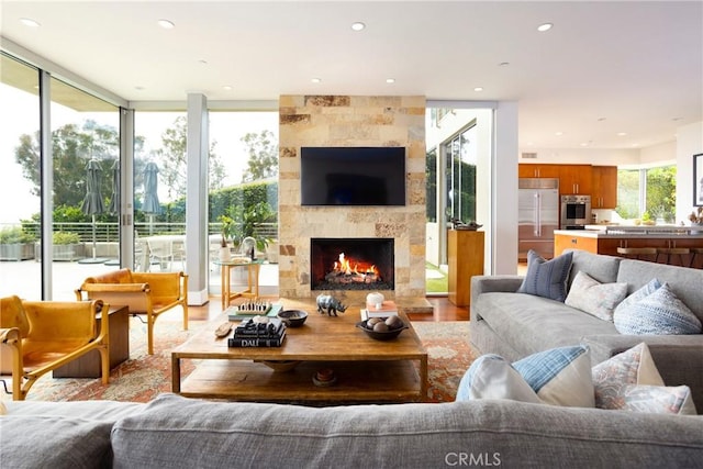 living room with floor to ceiling windows, a large fireplace, wood finished floors, and recessed lighting