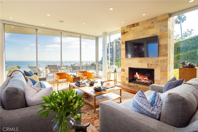 living room with wood-type flooring, a tiled fireplace, a water view, and a wall of windows