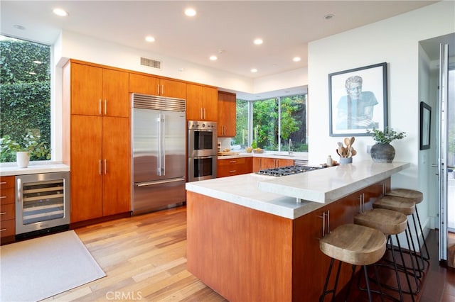 kitchen with beverage cooler, stainless steel appliances, light hardwood / wood-style floors, a kitchen breakfast bar, and kitchen peninsula