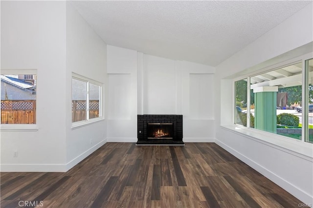 unfurnished living room featuring a brick fireplace, a textured ceiling, dark wood-type flooring, and vaulted ceiling