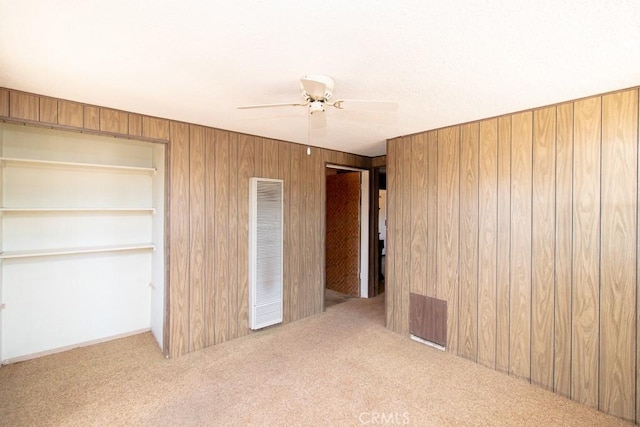 unfurnished bedroom with a ceiling fan, carpet floors, wooden walls, and visible vents