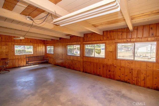 interior space featuring vaulted ceiling with beams, wood walls, and concrete floors