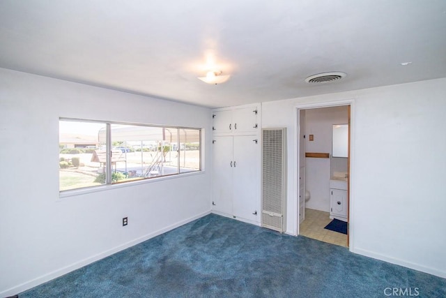 unfurnished bedroom featuring a heating unit, baseboards, carpet floors, visible vents, and a closet