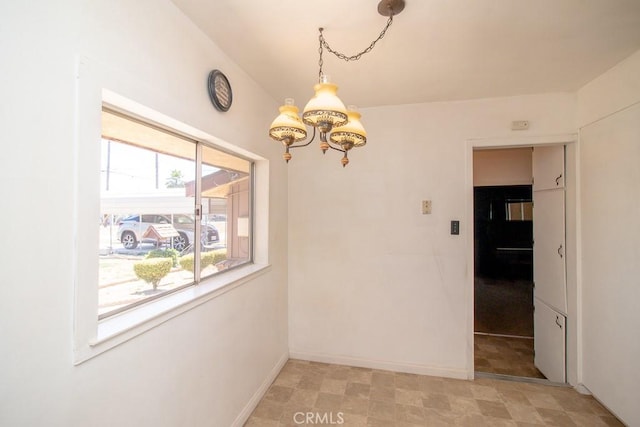 unfurnished dining area featuring an inviting chandelier and baseboards