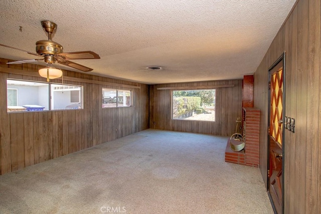 empty room featuring a textured ceiling, carpet floors, wooden walls, visible vents, and ceiling fan