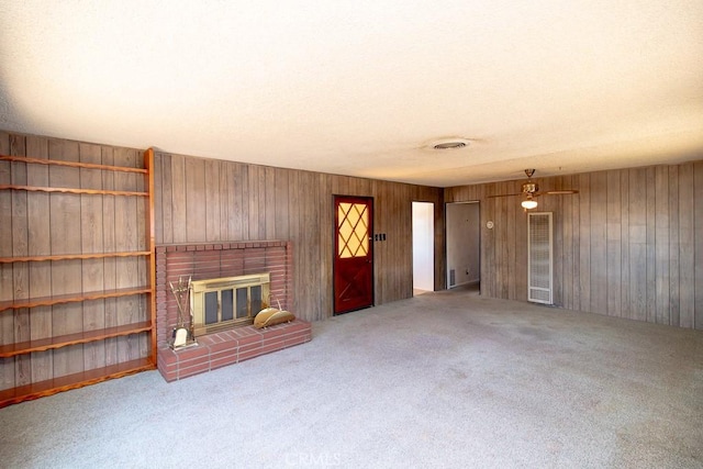 unfurnished living room with visible vents, wood walls, carpet flooring, and a fireplace