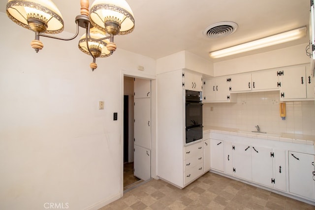 kitchen featuring pendant lighting, decorative backsplash, tile counters, white cabinets, and black oven