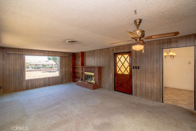 unfurnished living room featuring carpet, a fireplace, wooden walls, a textured ceiling, and ceiling fan with notable chandelier