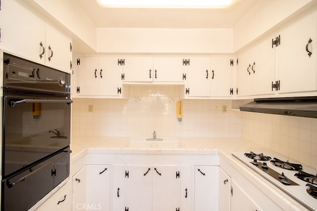 kitchen featuring tasteful backsplash, tile countertops, sink, white gas cooktop, and white cabinets