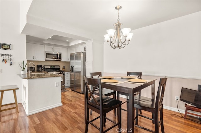 dining room featuring light hardwood / wood-style floors, a notable chandelier, sink, and a raised ceiling