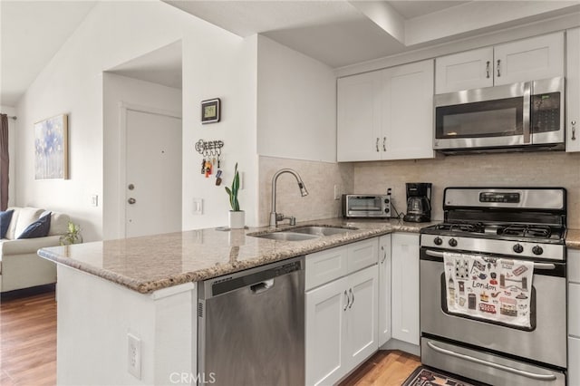 kitchen featuring light wood-type flooring, kitchen peninsula, backsplash, appliances with stainless steel finishes, and sink