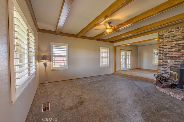 unfurnished living room featuring ceiling fan, beam ceiling, carpet flooring, and a wood stove