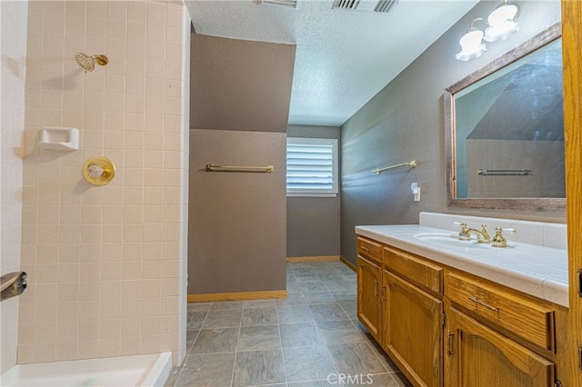 bathroom featuring vanity, a textured ceiling, and tiled shower