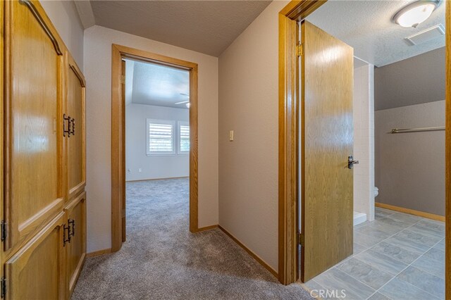 corridor with a textured ceiling and light carpet