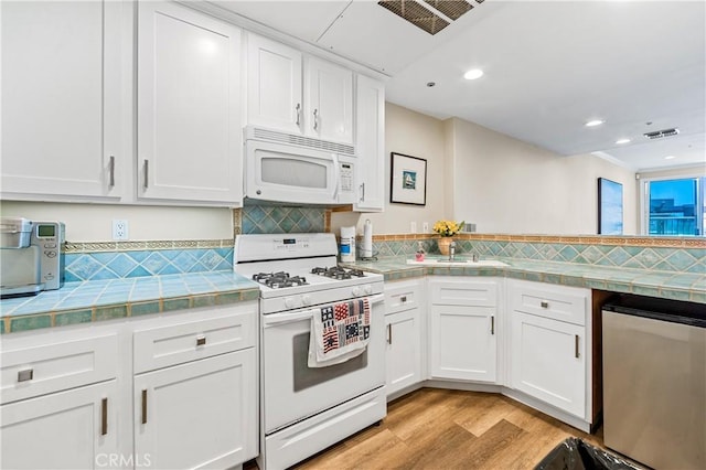 kitchen with white appliances, visible vents, white cabinetry, tile counters, and light wood finished floors