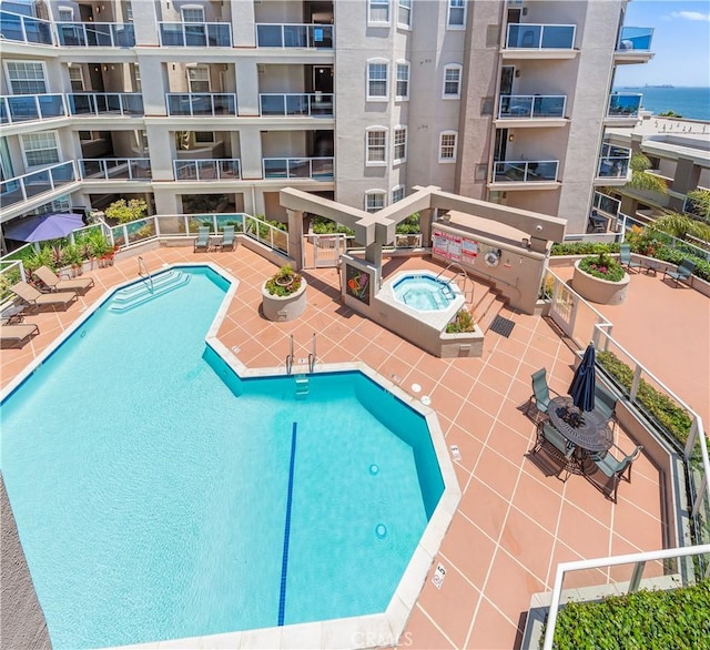 pool featuring a water view, a patio area, grilling area, and a community hot tub