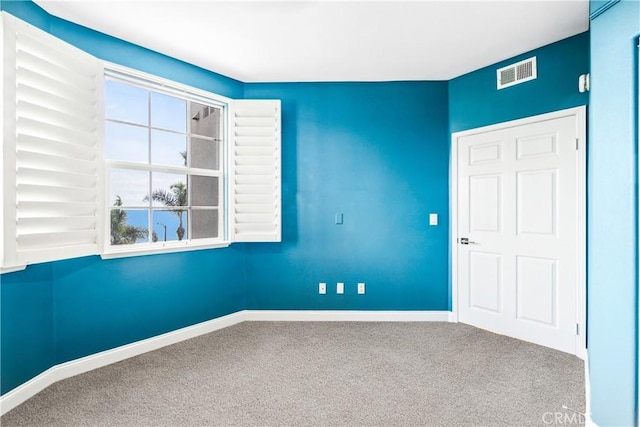 unfurnished room with carpet, visible vents, and baseboards