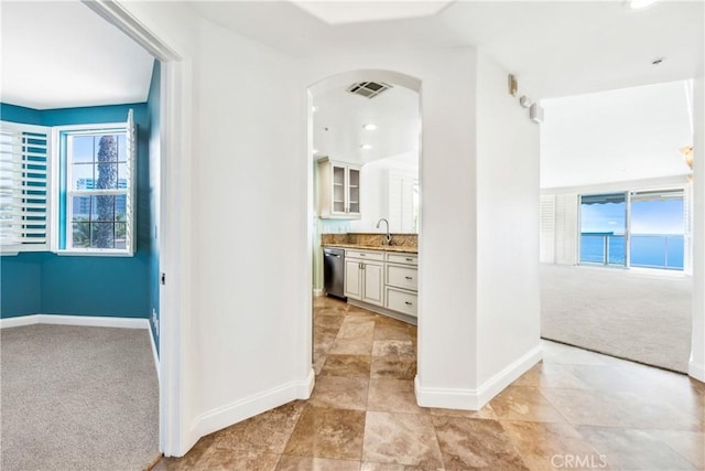 corridor featuring light carpet, baseboards, visible vents, arched walkways, and a sink