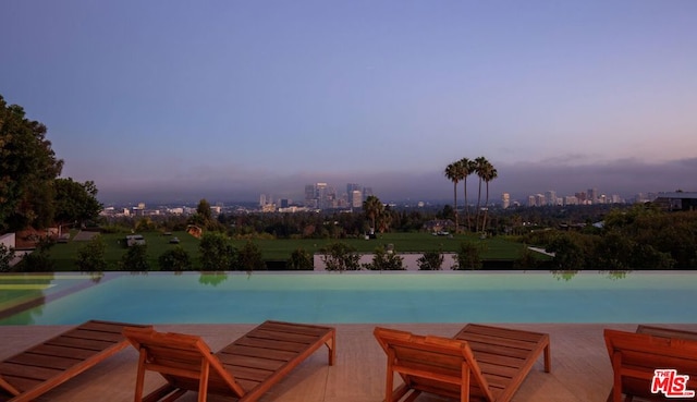 pool at dusk featuring a water view and a patio area