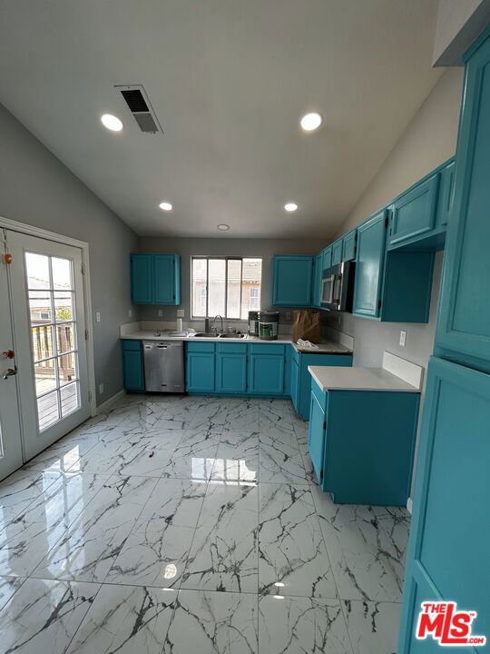 kitchen with blue cabinetry, lofted ceiling, appliances with stainless steel finishes, and a wealth of natural light