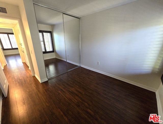 unfurnished bedroom with dark hardwood / wood-style flooring and a closet